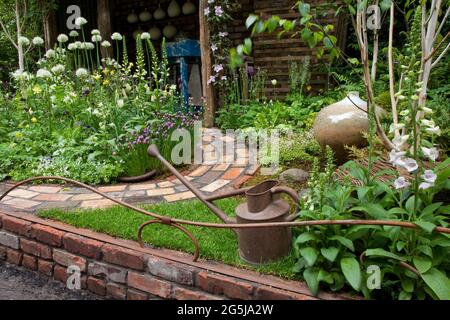 Pottering in North Cumbria' featuring a brick path leading to a lean-to pottery, crystalline glazed pot, spring planting and waterin can. Stock Photo