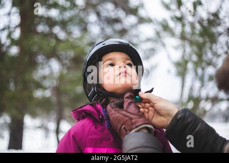 Mature man helping daughter wearing helmet during winter Stock Photo