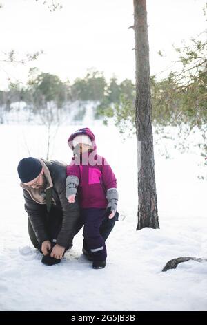 Mature man helping daughter wearing shoe on snow Stock Photo