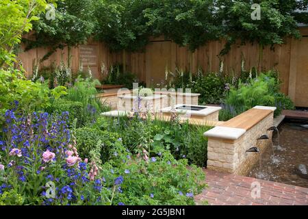 Brick seating area with timber benches and fire pit, raised herb bed, waterfall pond water feature Stock Photo