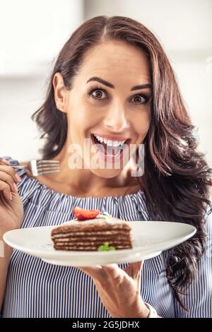 Woman enthusiastic about sweet delight of layered cake holding a fork and a plate in her hands. Stock Photo