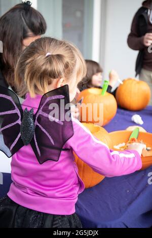 Caucasian family carving pumpkins on Halloween day, on a blue tablecloth to make  jack'o Lanterns dressed in spooky costumes. Vertical shot. Stock Photo