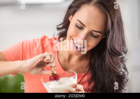 Young woman enjoys dipping fresh strawberry into a bowl of whipped cream. Stock Photo