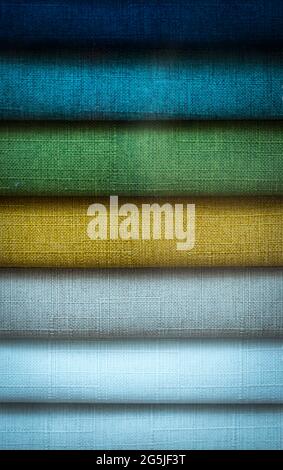 Rolls of colored fabric are neatly stacked in a row on the store shelves, close-up. Stock Photo