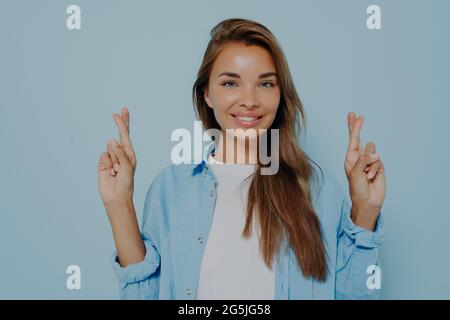 Joyful woman in casual clothes points up cross fingers Stock Photo