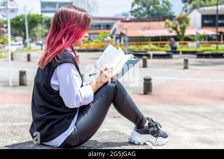 young latina woman sitting in outdoors writing on her notepad. Stock Photo