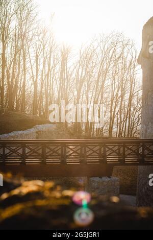 Wooden bridge connecting two parts of cobblestone Trencin castle with bright sun setting in background behind autumn trees Stock Photo