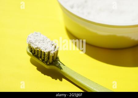 Green plastic toothbrush with tooth-powder on yellow table. Stock Photo