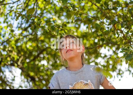 Defocused preteen blond girl on green tree summer background. Free happy childhood. Love nature. Out of focus Stock Photo