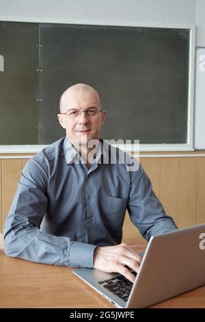 Successful male teacher sitting by workplace against blackboard Stock Photo