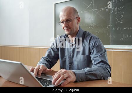 Contemporary teacher using laptop during online lesson in classroom Stock Photo