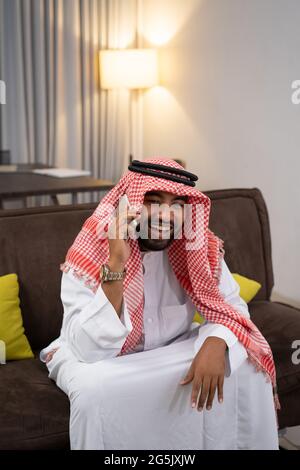 Arab businessman in a turban laughing while using a cellphone while sitting on the sofa Stock Photo