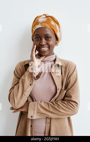 Vertical portrait of smiling African-American woman looking at camera while standing against white wall Stock Photo
