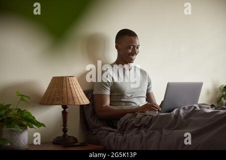 Smiling African man using a laptop in his bed at home Stock Photo