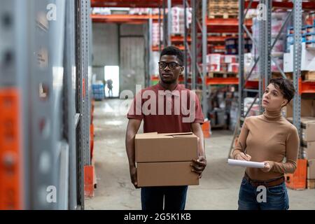 Two young intercultural workers of warehouse standing in aisle Stock Photo