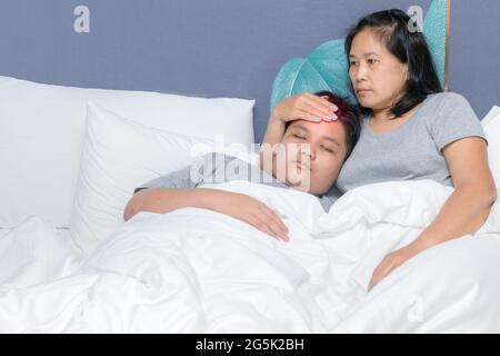 Mother puts her hand on forehead to measure the temperature of her son in bed. Sick boy lying with mother. concern and care concept Stock Photo