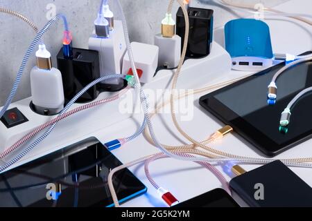 Smartphone Mobile Phone and tablets connected to Charging hub on the Table, micro usb   wires to chargers in sockets. Extension cord switch loaded wit Stock Photo