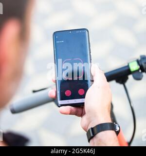 Close up of hand and smartphone, unlocking dockless electric scooter for rent with debranded generic phone app. Stock Photo