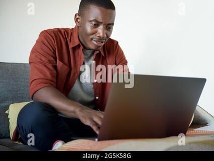 Young African man working remotely from home on a laptop Stock Photo