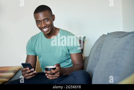 Smiling young African man texting over coffee at home Stock Photo