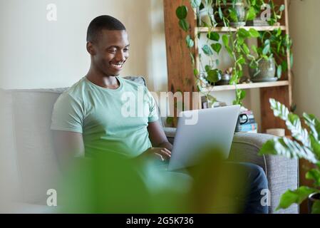 Smiling young African man using a laptop on his sofa Stock Photo