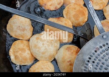 Many Kochuris are being fried in a frying pan. Kochuri, kachori of kachauri is a spicy snack, fried dumpling and a very popular street food in India. Stock Photo