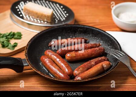 Tasty fried sausages in frying pan with Parmigiano and parsley, over wooden background Stock Photo