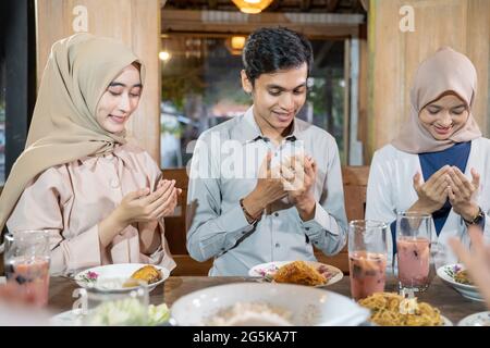a man and two women in veil pray together before eating while breaking their fast Stock Photo