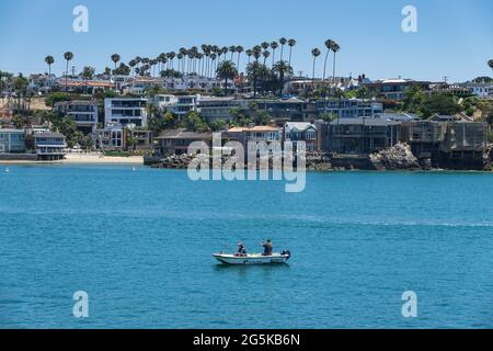 2 men fishing from a small boat in the Newport Beach Harbor entrance channel with luxury coastal homes in the background . California ; USA Stock Photo