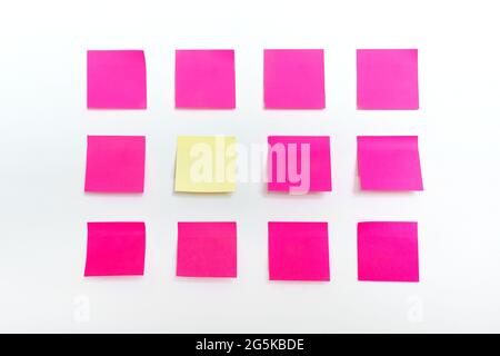 Rows of many colorful bright empty pink sticky paper notes and one stand of a kind stand yellow sticker isolated on white wall textured background Stock Photo