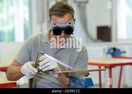 man wearing goggles while using gas torch on copper pipe Stock Photo