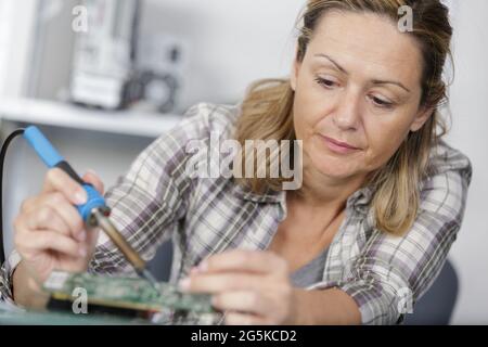 man helping woman soldering elements of circuit board Stock Photo