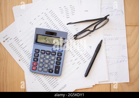 Calculator, glasses, pen and papers on wooden background. Top view flat lay business concept. Stock Photo