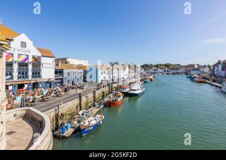 Tourists, boats moored quayside in Weymouth, a seaside town and popular holiday resort on the estuary of the River Wey, Dorset, south coast England Stock Photo