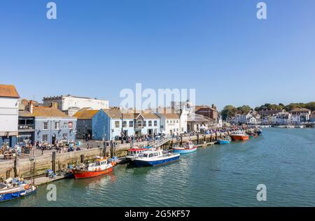 Tourists, boats moored quayside in Weymouth, a seaside town and popular holiday resort on the estuary of the River Wey, Dorset, south coast England Stock Photo