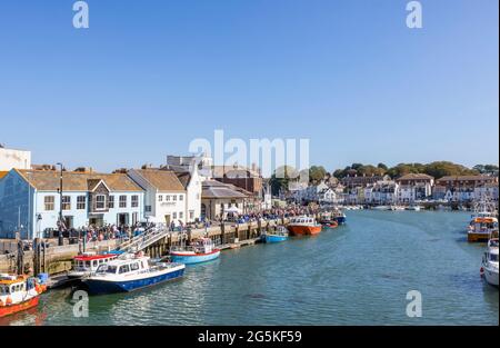 Tourists, boats moored quayside in Weymouth, a seaside town and popular holiday resort on the estuary of the River Wey, Dorset, south coast England Stock Photo