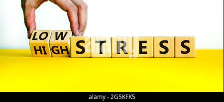 Low or high stress level symbol. Businessman turns wooden cubes and changes words high stress to low stress. Beautiful yellow table, white background. Stock Photo