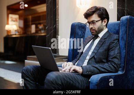 Portrait of successful Middle-Eastern businessman using laptop while working in hotel lobby on business trip, copy space Stock Photo