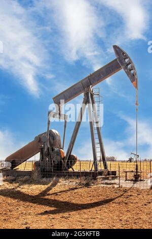 Oilfield pump jack out in summer red dirt field on bright day with shadow and a few whispy clouds in blue sky Stock Photo