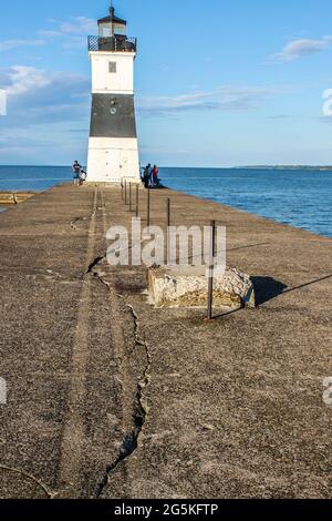 Old metal black and white lighthouse at end of cracked pier near Erie PA with people fishing and standing around  out at the end with Lake Erie in the Stock Photo