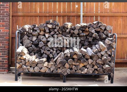Stacked weathered firewood in racks - part way through winter - against redwood privacy fence Stock Photo