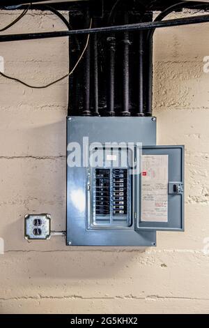 Stainless steel electrical circuit box open with circuits named by hand in basement on rough concrete block wall with conduit and ceiling and other pi Stock Photo