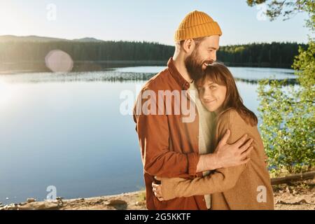 Young happy couple embracing each other standing on the nature with lake in the background Stock Photo