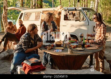 Group of friends having lunch at the table outdoors during their camping on the nature Stock Photo