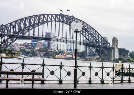 View of Sydney Harbour Bridge from the Circular Quay on a wet morning, with city in the distance and a ferry crossing over Stock Photo