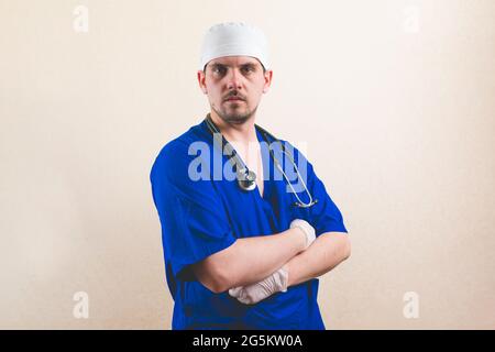 Young doctor portrait in blue suit with stethoscope and with his hands on his chest isolated on smooth background Stock Photo