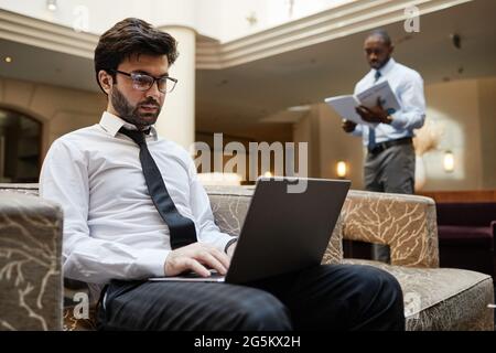 Portrait of successful Middle-Eastern businessman using laptop while working in hotel lounge, copy space Stock Photo
