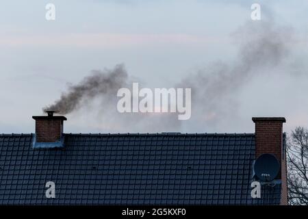 A roof with two chimneys on it. In one of the chimneys there is a pipe mounted on it were a lot of black polluting smoke is coming out or rising up fr Stock Photo