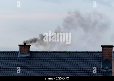 A roof with two chimneys on it. In one of the chimneys there is a pipe mounted on it were a lot of black polluting smoke is coming out or rising up fr Stock Photo