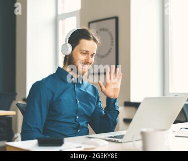 Young happy man office worker in headphones smiling during video call Stock Photo